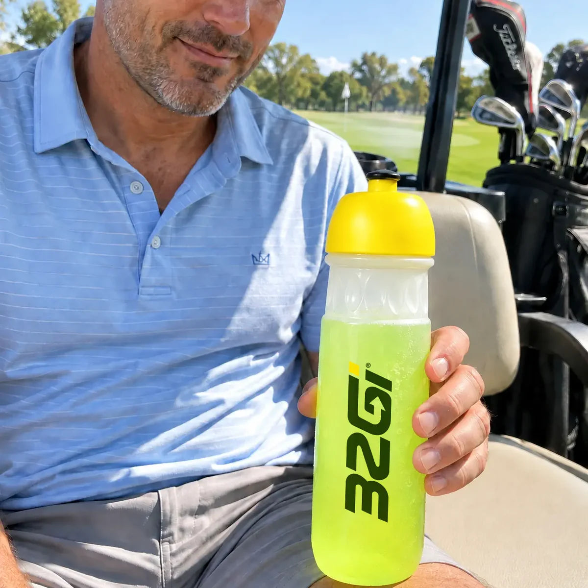 A golfer in the cart holding a 32GI bottle of Hydrate Lime, clubs behind him